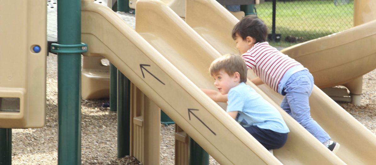 Two children on the slide at the playground in the University of Delaware Early Learning Center