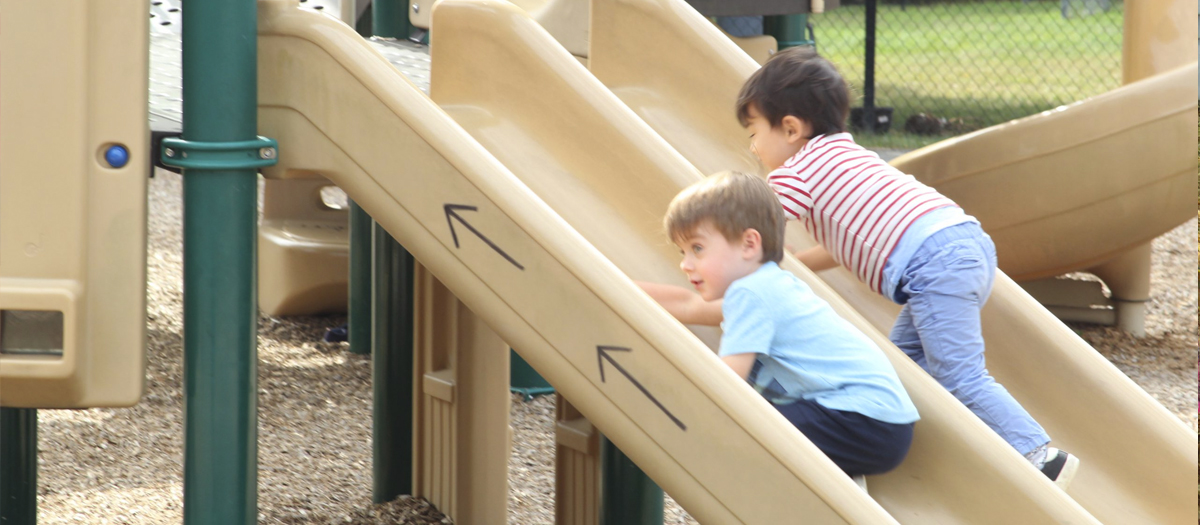 Two children on the slide at the playground in the University of Delaware Early Learning Center